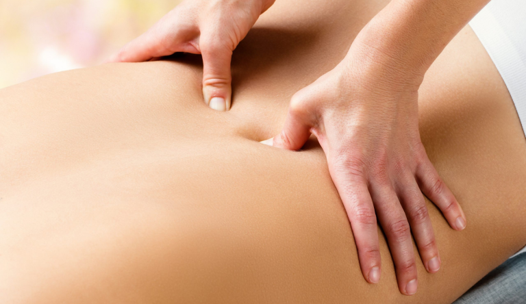 Zwei Hände drücken sanft auf den unteren Rücken einer liegenden Person während einer Behandlung. Manuelle Rückenbehandlung in der Naturheilpraxis Karin Kossek in Duisburg.